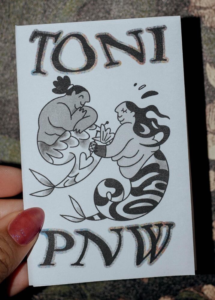 Untitled A photo of a zine titled "TONI PNW" There are two drawn mermaids, one getting and one receiving a tattoo.