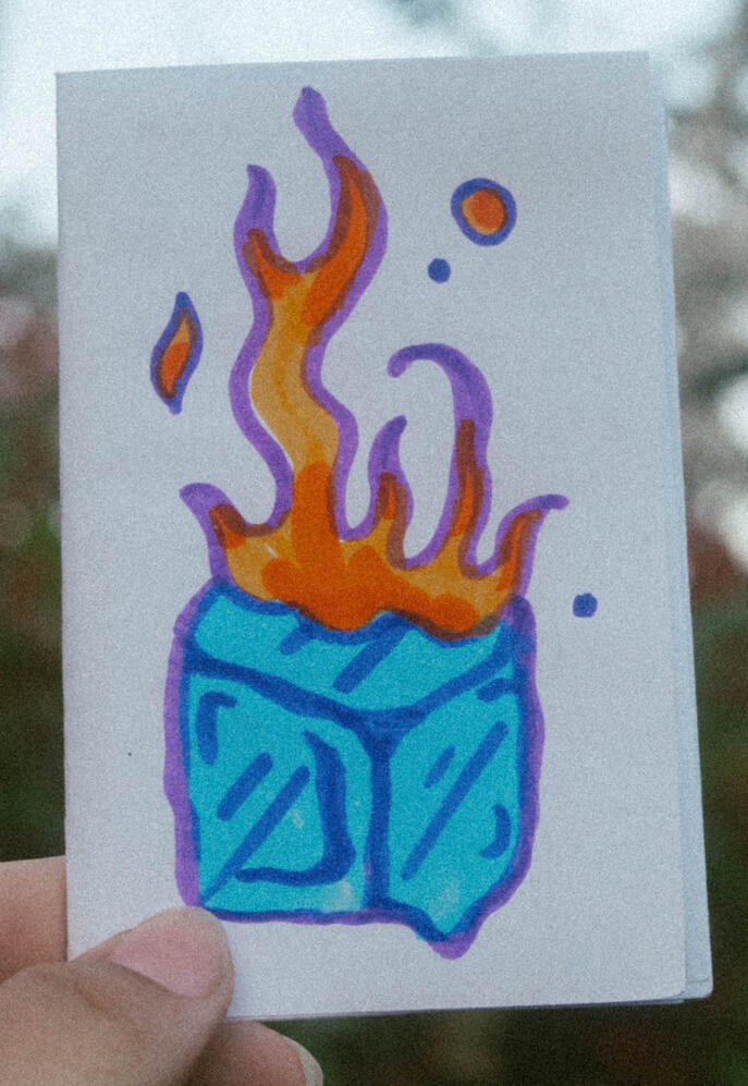 A photo of a zine cover with an ice cube on fire. This zine is titled "No Mas Miedo"