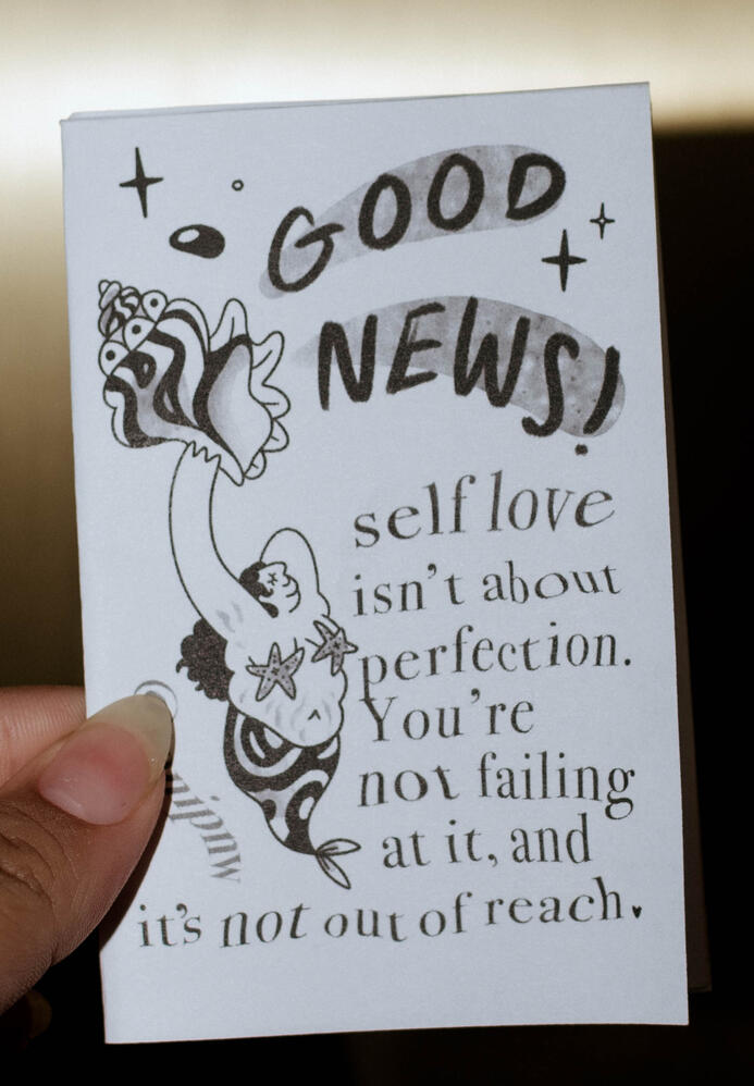 A photo of a zine titled "Good News!" smaller text says "self love isn't about perfection. You're not failing at it, and it's not out of reach."