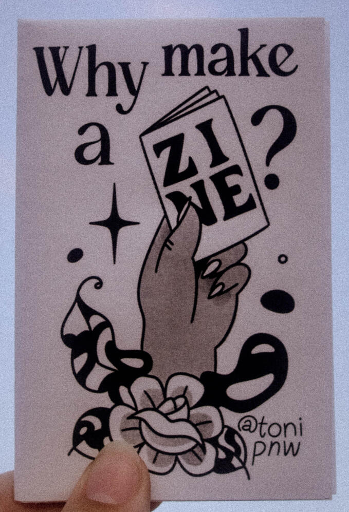 A photo of a zine cover depicting a hand holding a zine. This zine is titled "Why Make A Zine?"